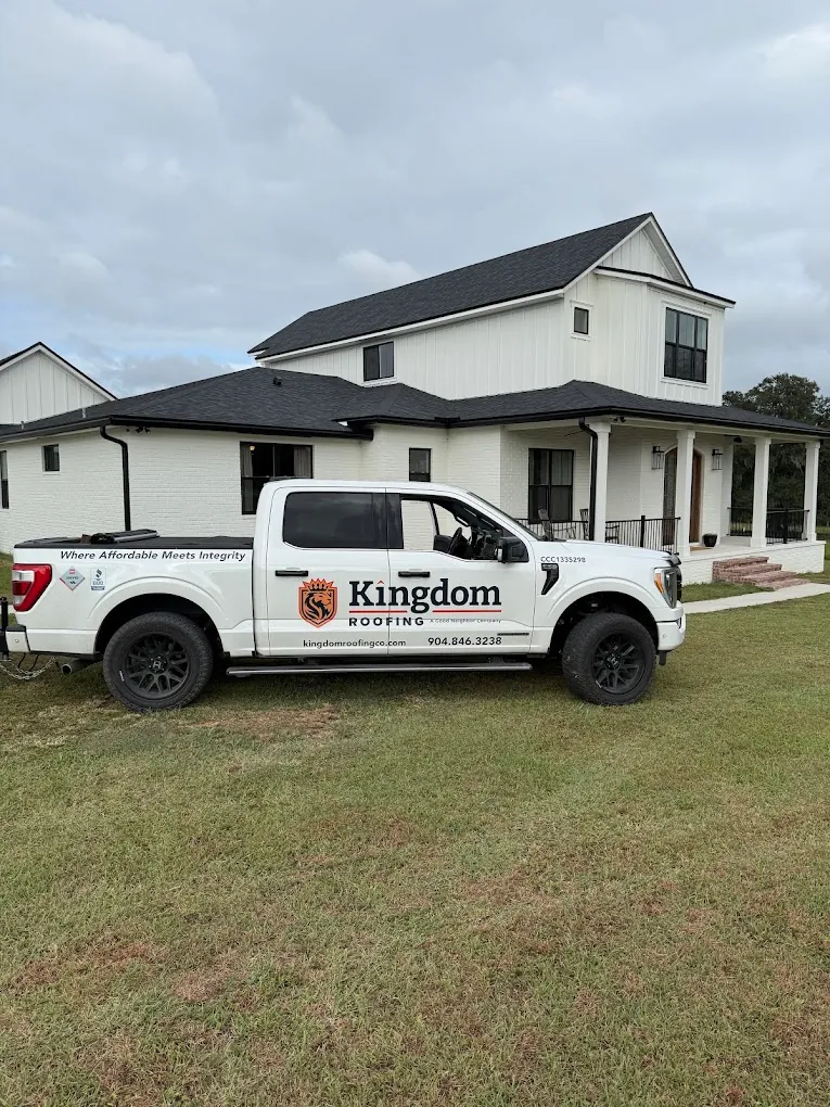 Kingdom Roofing service truck parked beside a white home with a dark roof.